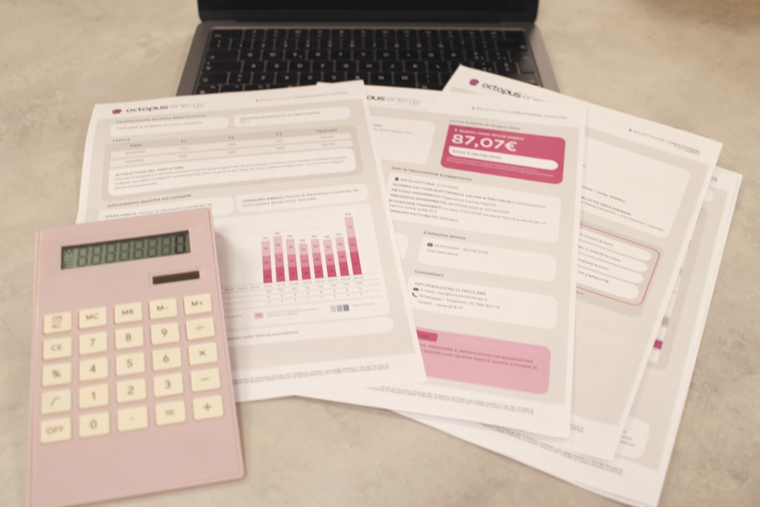 A pink calculator sits on a desk beside several printed bills and a laptop