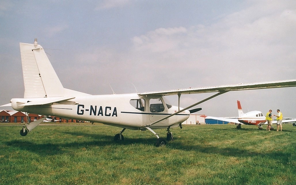 A white single-engine airplane with "G-NACA" on the tail parked on grass