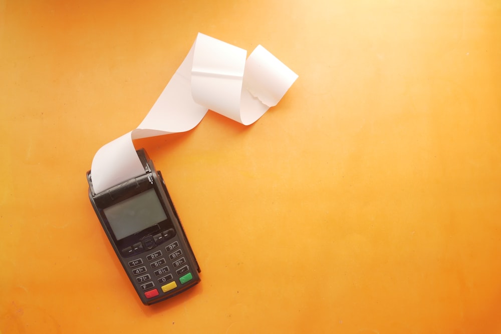 A black payment terminal with a long paper receipt on an orange surface