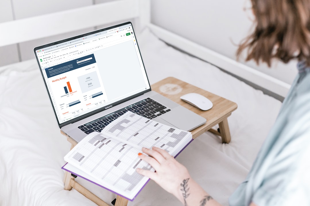 Person working on a laptop with a monthly budget spreadsheet open, printed pages on a lap desk