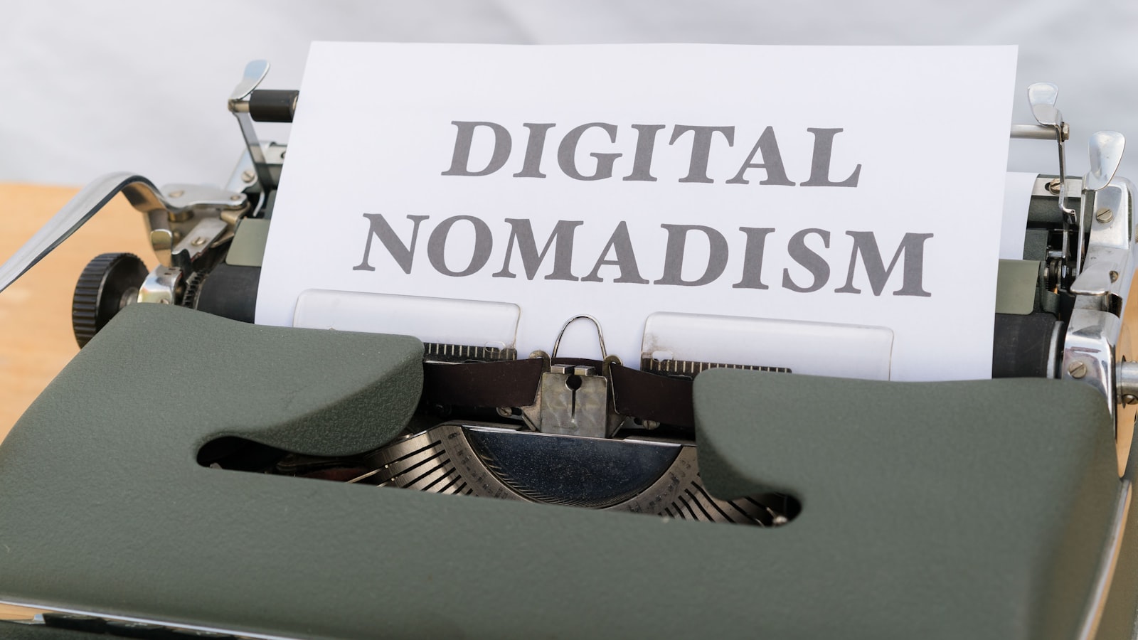 A vintage olive-green typewriter holds a white page reading "DIGITAL NOMADISM" in bold caps