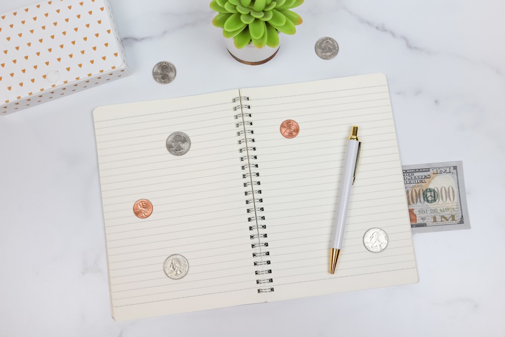An open notebook with coins, a pen, and a one million dollar bill on a white surface