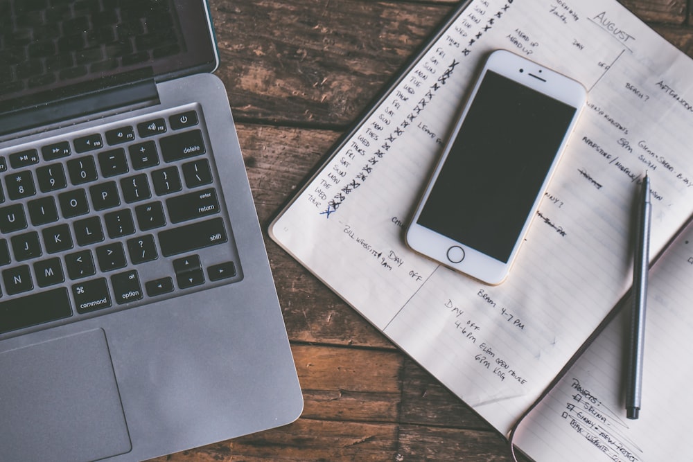 Overhead view of a laptop, smartphone on an open planner, and pen on wood