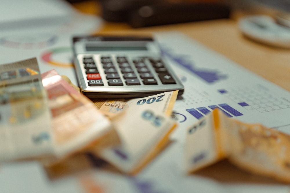 A calculator and stacks of euro banknotes sit on top of financial charts