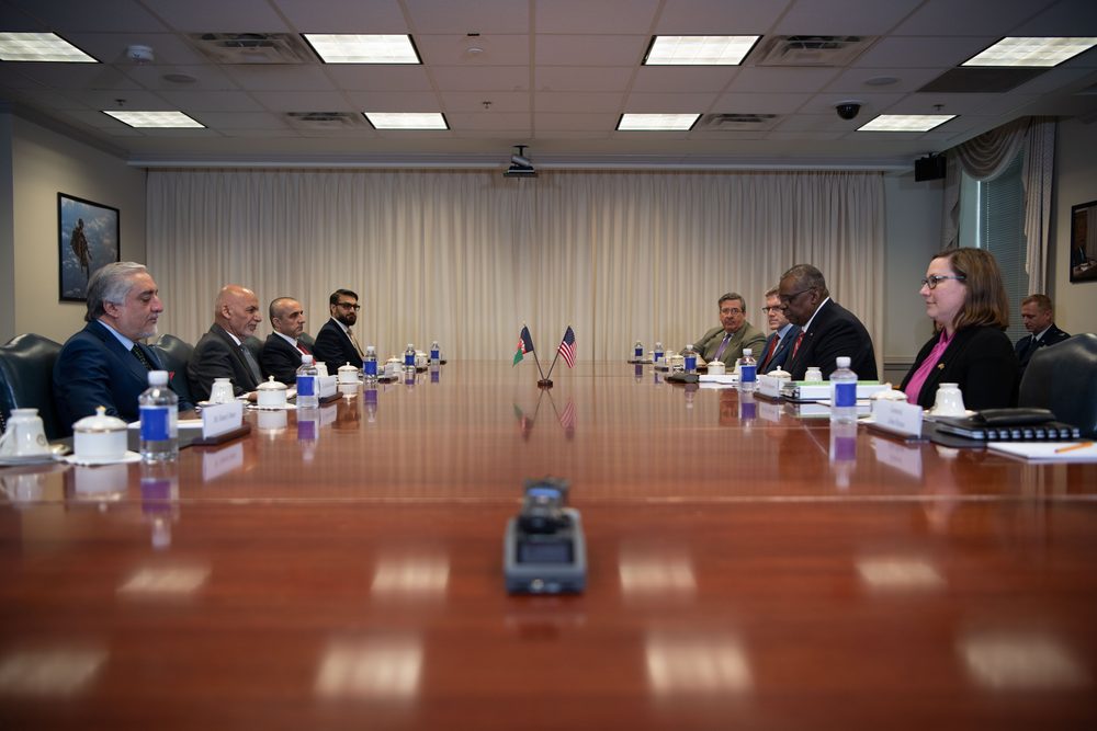 Two groups of people sit facing each other across a long, polished wooden conference table
