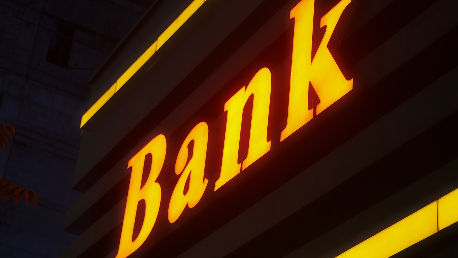 A low-angle, nighttime shot of an illuminated yellow sign that reads "Bank"