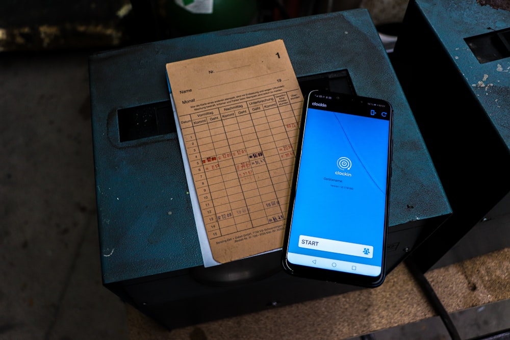 A smartphone and a paper timesheet rest on a dark blue metal surface