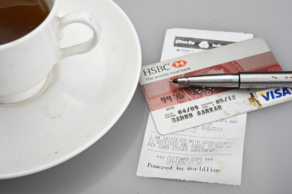 A cup of tea and saucer beside a credit card, pen, and receipt