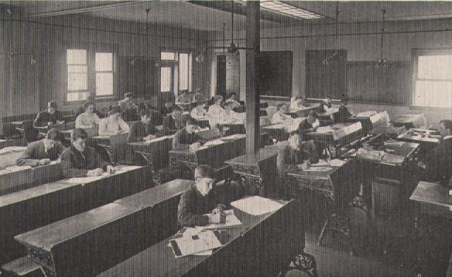 Vintage black-and-white photo of a large classroom filled with students seated at wooden desks