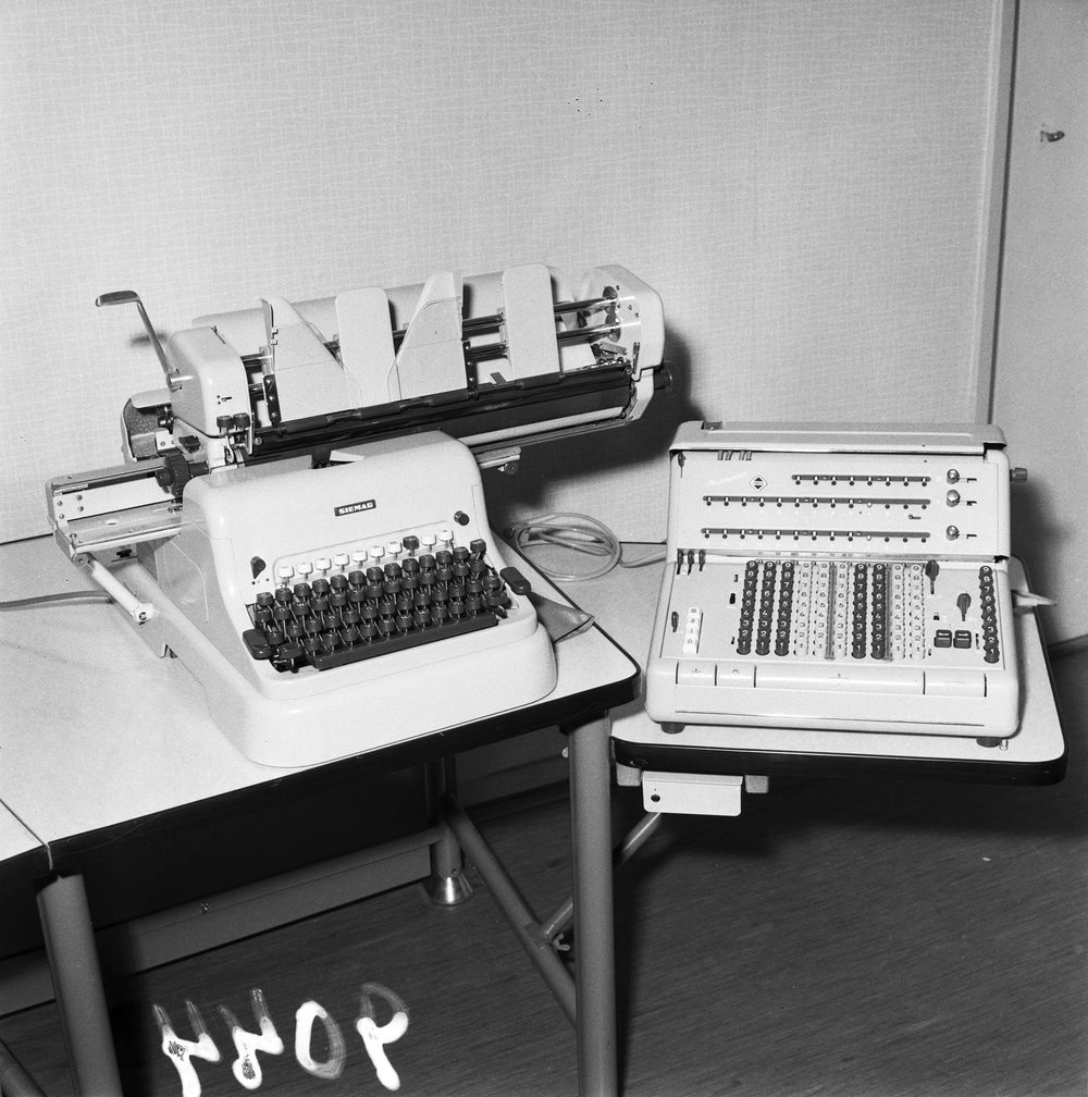 An electric accounting machine and a mechanical calculator sit on separate desks