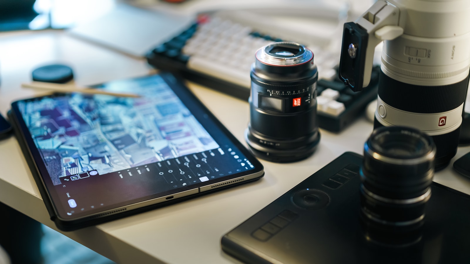 A tablet, camera lenses, and a drawing tablet are on a desk